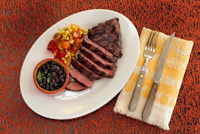 This Aug. 4, 2016 photo shows skirt steak with beer-braised black beans and corn salsa, styled by Sarah Abrams, displayed at the Institute of Culinary Education in New York. This dish is from a recipe by Elizabeth Karmel. (AP Photo/Richard Drew)