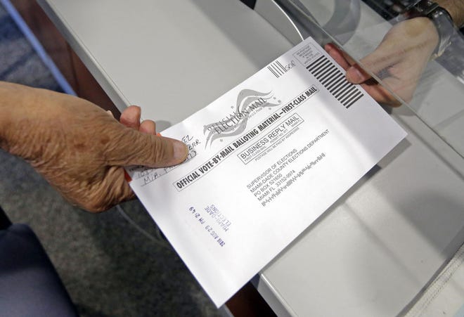 A voter hands his absentee ballot to a Miami-Dade County elections official, Monday. Florida voters will go to the polls Tuesday and select the nominees for U.S. Senate, decide whether to amend the state constitution to give a property tax break to promote solar energy and have a say in who should represent them in the U.S. House.