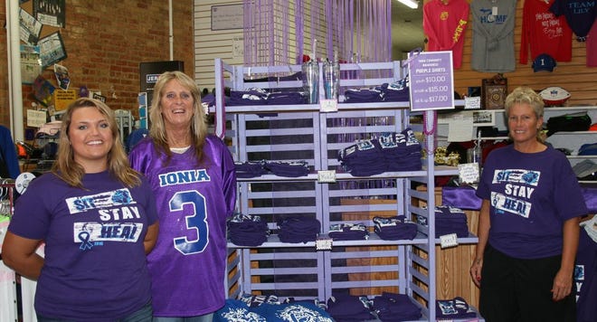 Jessa Delo, left, Christine Engle, center, and "Wrecker," right, stand near the display of Purple Week gear at Wrecker's Tuesday.