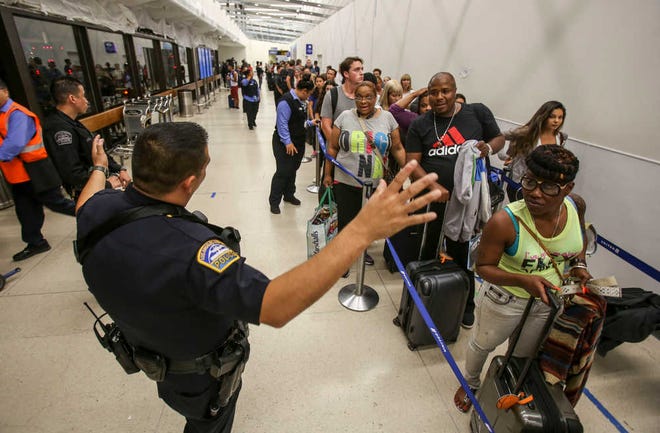 Police officers stand guard as passengers wait in line at Terminal 7 in Los Angeles International Airport, Sunday, Aug. 28, 2016. Reports of a gunman opening fire that turned out to be false caused panicked evacuations at Los Angeles International Airport on Sunday night, while flights to and from the airport saw major delays. Passengers who fled had to be rescreened through security. A search through terminals brought no evidence of a gunman or shots fired, Los Angeles police spokesman Andy Neiman said. (AP Photo/Ringo H.W. Chiu)