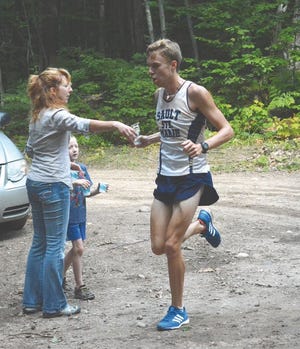 Sault High senior Chris Larson accepts a cup of water during a Time Trials run in Bay Mills last Friday. Larson broke the team 5-mile time trials record, previously held by Tony Abramson. The Blue Devils boys and girls teams begin a new season today at the Ogemaw Heights Invitational.