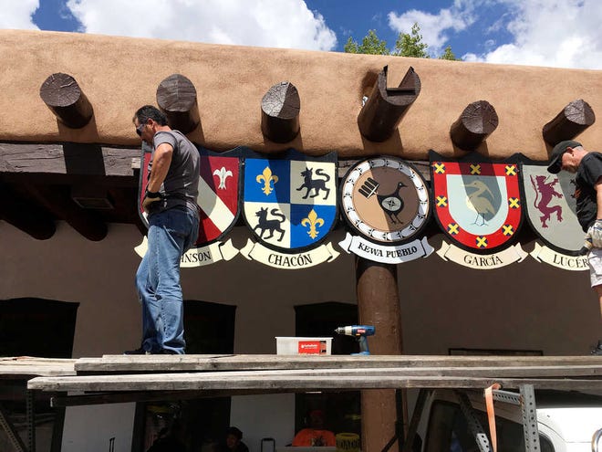This Sept. 1, 2016 photo shows Organizers of the Santa Fe Fiesta in Santa Fe, N.M., place shields of the last names of original Spanish settler families on the Palace of the Governors while American Indian jewelers sell items below. For centuries, northern New Mexico Hispanic residents have held an elaborate festival in Santa Fe in honor of Spanish conquistador Don Diego De Vargas' who reclaimed the city following an American Indian revolt. But after 301 years, an emboldened group of Native American activists say it's time to change a celebration centered around the conquest of New Mexico's Pueblo tribes. (AP Photo/Russell Contreras)