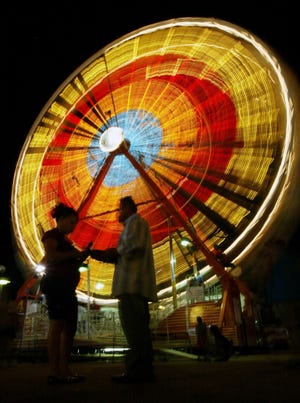 Fairgoers are silhouetted against the ferris wheel at the north end of the midway on Saturday night at the Kansas State Fair. (Lindsey Bauman)