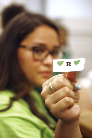 Middletown High School junior Kerollayne Lemos, 17, holds up one of the stickers that were sold at the school Friday during ‘Green Out’ to raise money for the family of Ramon Arroyo, 7, who died in a fire on Monday.