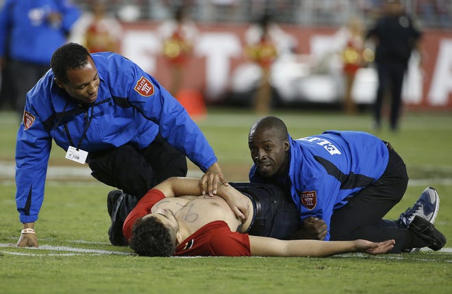 A fan is tackled by security officers during the second half of the San Francisco 49ers-Los Angeles Rams game Monday night. Announcer Kevin Harlan's call of the fan's movements has become a trending topic online. Associated Press/Tony Avelar