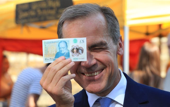 Bank of England Governor Mark Carney holds a new plastic £5 note as he visits Whitecross Street market in London, Tuesday, Sept. 13, 2016. The polymer note is said by the Bank of England to be cleaner, safer and stronger than paper notes, lasting around five years longer. (Jonathan Brady/PA via AP)