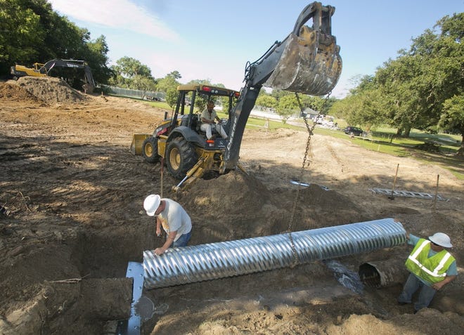 Construction workers install a section of drain pipe for a retention pond. (File)