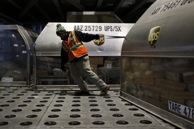 A UPS worker pulls a container full of packages across a floor embedded with casters at Worldport in Louisville, Kentucky. UPS plans to add 95,000 workers to meet the 2016 holiday season demand from online shopping. The Associated Press