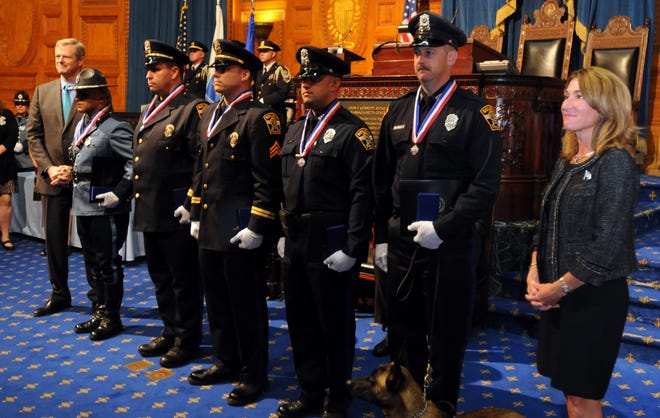 Retired Bourne police Officer Jared MacDonald, second from right, with his service dog, Bullet, at his feet, received the Medal of Honor on Thursday during a Statehouse ceremony honoring police for bravery. Officers who received the Medal of Valor for the same 2015 incident were, from left, state Trooper Nathan R. Monteiro, Bourne Detective Sgt. John R. Stowe Jr., Sgt. Wallace J. Perry IV and Officer Joshua A. Parsons. Gov. Charlie Baker is at far left and Lt. Gov. Karyn Polito is at right. Steve Haines/Cape Cod Times