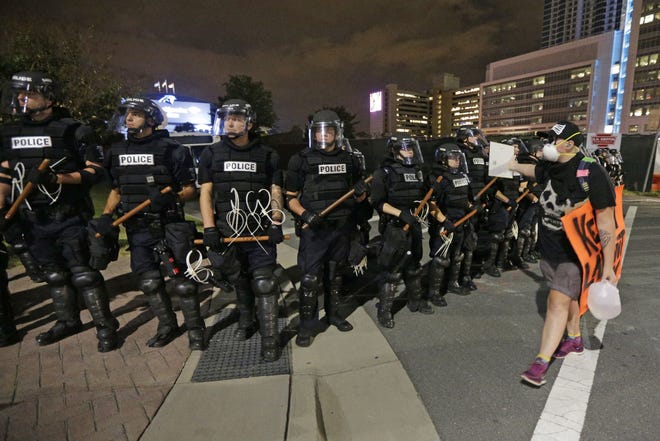 A protester walks in front of a line of police officers blocking the access road to I-277 on the third night of protests in Charlotte, N.C. Thursday, Sept. 22, 2016, following Tuesday's fatal police shooting of Keith Lamont Scott. (AP Photo/Chuck Burton)