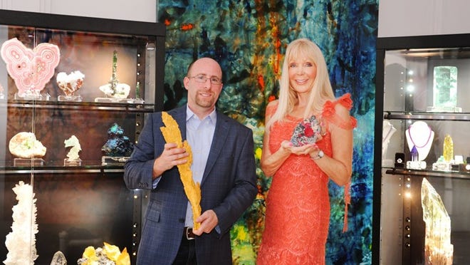 Robert Lavinsky, owner of The Arkenstone, shows minerals and gems Friday at Ildiko Contemporary Fine Art Gallery, by Ildiko Varga’s paintings. He holds the “Thunderbolt,” a long, jagged gold piece valued at more than $1 million, while Varga shows a Rhodochrosite from an old silver mine.