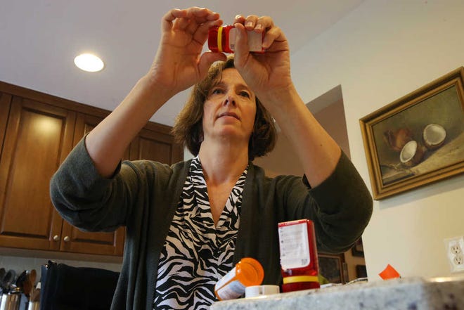 In this Sunday, Sept. 18, 2016, photo, Shelley Ewalt sits in her home, in Princeton, N.J., near an open amber-colored CVS pharmacy prescription bottle, as she opens one of two uniquely designed red ones from Target. After CVS took over operation of Target's drugstores earlier this year, distraught customers have been asking the drugstore chain to bring back the retailer's red prescription bottles, which came with color-coded rings, labeling on the top and prescription information that was easier to read. Ewalt tweeted to the drugstore chain, asking if there was any chance they might return to the design of the Target bottles, which she found easier to open. (AP Photo/Mel Evans)