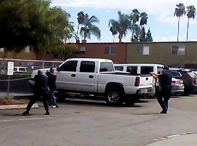 In this Tuesday, Sept. 27, 2016 frame from video provided by the El Cajon Police Department, a man, second from left, faces police officers in El Cajon, Calif. The man reportedly acting erratically at a strip mall in suburban San Diego was shot and killed by police after pulling an object from his pocket, pointing it at officers and assuming a "shooting stance," authorities said. Some protesters claimed the man was shot with his hands raised, but police disputed that and produced the frame from cellphone video taken by a witness that appeared to show the man in the "shooting stance" as two officers approached with weapons drawn. (El Cajon Police Department via AP)