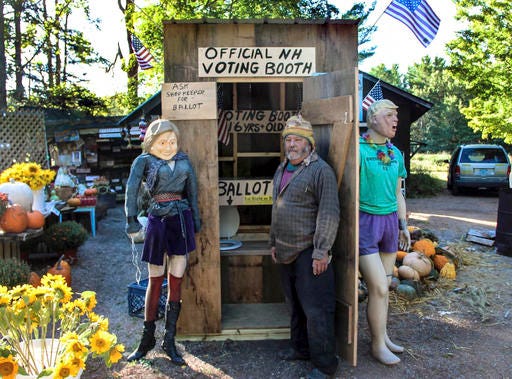 Chris Owens stands beside his outhouse-turned-voting booth at Owens Truck Farm in Ashland, N.H. Manikins of presidential candidates Hillary Clinton and Donald Trump hang outside the booth, while ballots are deposited into side-by-side toilets inside the booth.