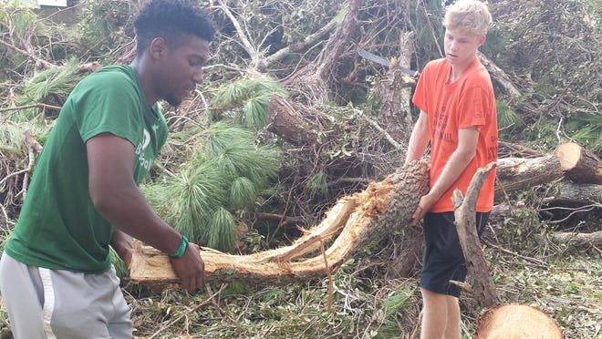 DeLand's Brandon Castle and Spruce Creek's Parker Fraine remove a log from a Port Orange home on Monday. Six local baseball players worked on clearing the backyard of 68-year-old Betty Johnson. News-Journal/Chris Boyle