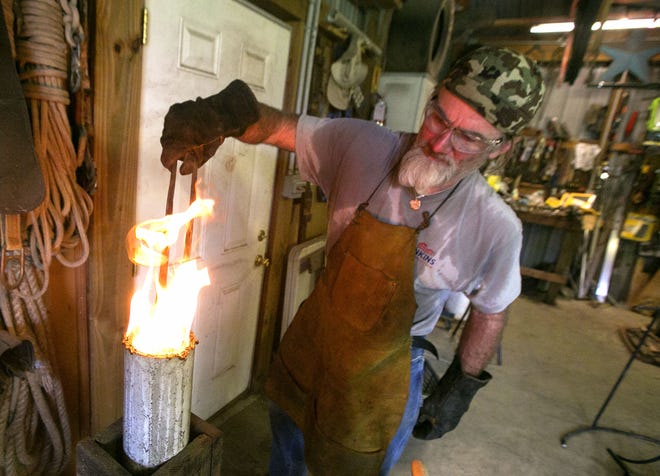 Blacksmith Keith Hill dips his blade into oil to temper it as he works forging a knife in his shop at his Ocklawaha on Monday. Hill competed in the History channel show "Forged in Fire." (Alan Youngblood/Star-Banner)