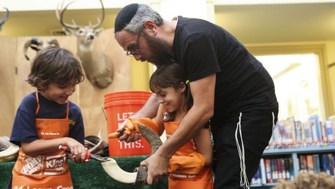 Rabbi Aron Rabin teaches Ari Zetouni, left, and Brea Siegel how to make a shofar at The Society of the Four Arts Children’s Library.
