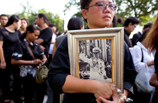 A Thai woman holds on to a portrait of Thai King Bhumibol Adulyadej in a line to offer condolences for the king at Grand Palace in Bangkok, Thailand, Friday, Oct. 14, 2016. Grieving Thais went to work dressed mostly in black Friday morning, just hours after the palace announced the death of their beloved King Bhumibol, the politically fractious country's unifying figure and the world's longest-reigning monarch.(AP Photo/ Gemunu Amarasinghe)