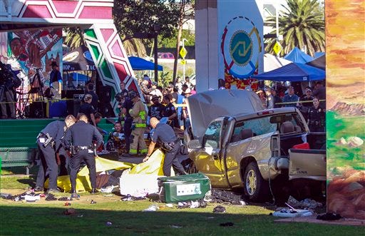 Police cover the bodies of people that were killed when a pickup truck landed on them after it flew off a ramp to the San Diego Coronado Bridge as paramedics prepare to put an injured man on a gurney, background, at Chicano Park in San Diego on Saturday.