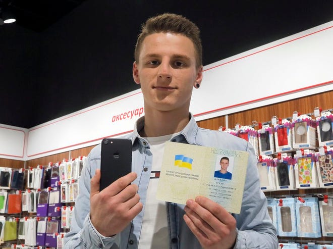A young man shows his passport giving his name as iPhone Sim (seven), and a new iPhone 7 in an electronics shop in Kiev, Ukraine, Friday, Oct. 28, 2016. A A computer company in Kiev announced that it will give a new iPhone 7 to anybody who officially changes their name to iPhone Seven. (AP Photo/Efrem Lukatsky)
