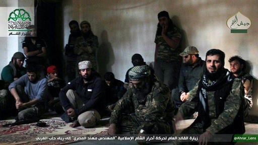 This picture posted, Sunday, Oct. 30, 2016, by the Syrian militant group Ahrar al-Sham, shows the general commander of Ahrar al-sham, Mohannad al-Masri, center, visiting fighters in rural western Aleppo, Syria. An insurgent alliance, known as the Army of Conquest and which includes an al-Qaida-linked group, attacked western Aleppo, aiming to breach a months-long siege on the rebel-held eastern side of the city. (Militant UGC via AP)