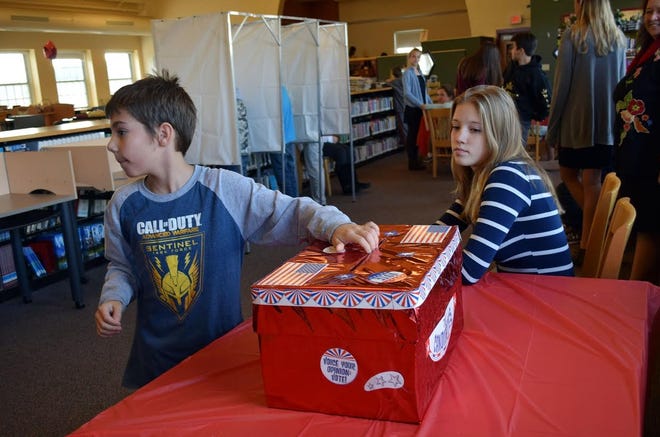 As WJHS student Vivianne Brousseau (at right) monitors the ballot box, student Alan Woodman deposits his ballot. In the background to the left are three voting booths with a registration area in the far background.

Photo by Reg Bennett