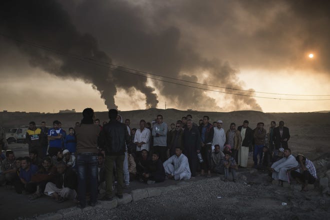 Men are held by Iraqi national security agents, to be interrogated at a checkpoint, as oil fields burn in Qayara, south of Mosul, Iraq, on Saturday. (AP Photo/Felipe Dana)