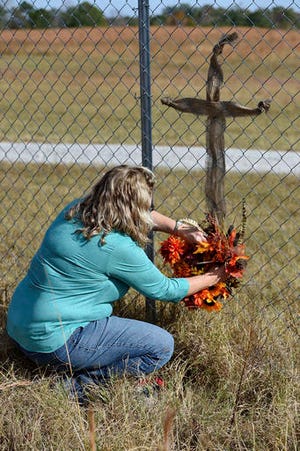 JoAnn McKinney, a local resident, prepares a cross on the fence of Todd Kohlhepp's property in Woodruff, S.C. Sunday, Nov. 6, 2016. Authorities have charged Kohlhepp, 45, with four counts of murder in the deaths of four people in 2003 at the Superbike Motorsports motorcycle shop. His alleged role in those killings was uncovered, authorities said, after the woman was found last week in a locked metal container on Kohlhepp's property in rural Woodruff. (AP Photo/Richard Shiro)