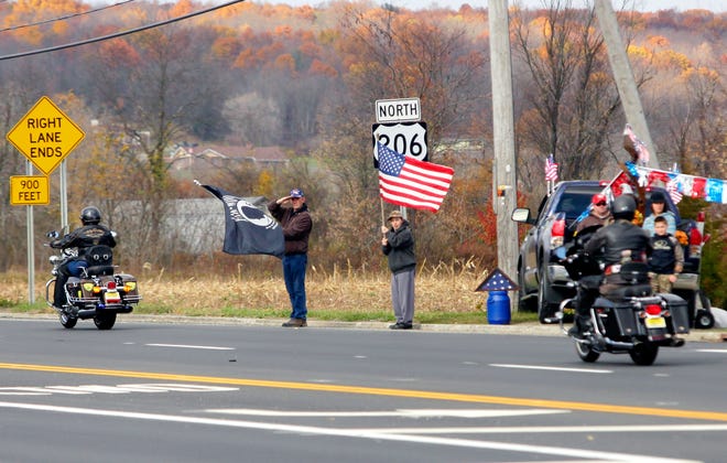 Photo by Tracy Klimek/New Jersey Herald - Standing on the side of Route 206 on Saturday in Frankford, a man holds the POW flag and salutes while a boy holds an American flag as motorcycles pass by escorting the remains of Korean War soldier William V. Giovanniello to bring him home to rest among his family in Port Jervis, N.Y.