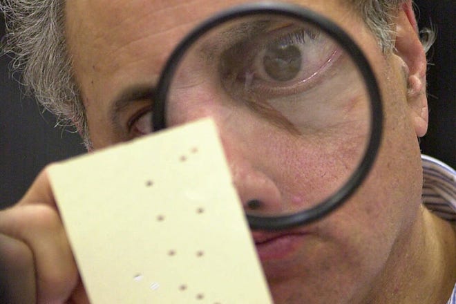 In this Nov. 24, 2000 file photo, Broward County canvassing board member Judge Robert Rosenberg uses a magnifying glass to examine a disputed ballot at the Broward County Courthouse in Fort Lauderdale (AP Photo/Alan Diaz, File)