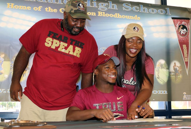 Auburndale senior Chauncy Smart signs with Florida State on Wednesday in the Auburndale High School library as his stepfathe, Rodney Copeland, and his mother, Tamisha Copeland, look on. ROY FUOCO/THE LEDGER