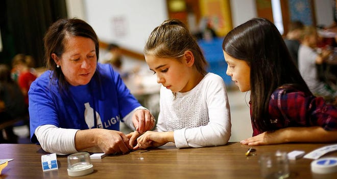 Sydney Dunn, 10, and Sophia Suplee, 9, both fourth-graders at the Hamilton School in Weymouth, work on making small reading lights that fit in a jar. At left, Hamilton School alumna Liz Sylvester of Hingham helps them with the wiring on Wednesday, Nov. 9, 2016.