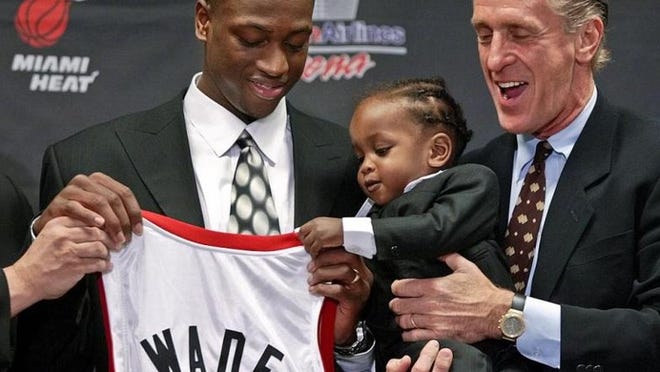 Dwyane Wade, left, former Marquette point guard and the fifth overall selection in the 2003 NBA draft, gets a little help holding up his jersey from his son Zaire, 16 months, as Miami Heat coach Pat Riley, right, holds him during a news conference introducing Wade Friday, June 27, 2003, in Miami. (AP Photo/Wilfredo Lee)