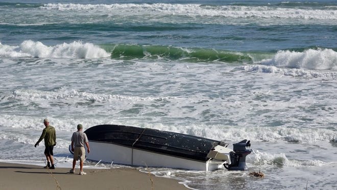 FWC officers attach a chain to a boat on the beach in Carlin Park Wednesday morning, November 9, 2016 after it capsized offshore. Two boaters were rescued and transported to a hospital. (Lannis Waters / The Palm Beach Post)