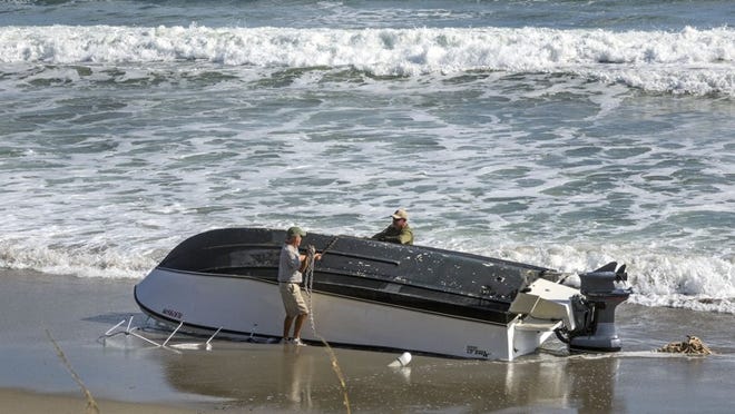A chain is attached to a boat overturned on the beach in Carlin Park in Jupiter on Wednesday morning, November 9, 2016 in preparation for towing it away after it capsized offshore. Two boaters were rescued and transported to a hospital. Both have died, the Florida Fish and Wildlife Conservation Commission said Thursday. (Lannis Waters / The Palm Beach Post)