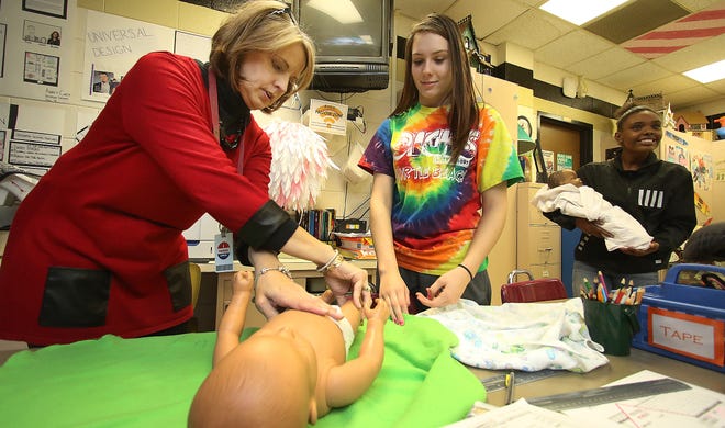 (L-R) Teacher Diane Gibson shows how to swaddle a newborn to Madison Kimsey, 15, along with Destynee Woodberry, 17, in family and consumer sciences class Tuesday afternoon at North Gaston High School. PHOTO MIKE HENSDILL/THE GAZETTE