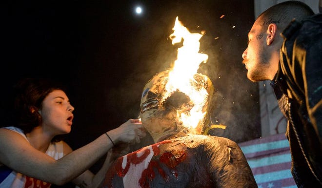 FILE - In this Wednesday, Nov. 9, 2016 file photo, a woman who identified herself as J. Stroh sets fire to an effigy of Donald Trump, as a man who identified himself as Blue Velvet blows on the flames, during an anti-Trump protest at Lee Circle in New Orleans. Jim Mullen, president of Allegheny College in Meadville, Pa., which awards a prize each year for civility in public life says, "We can all point to incidents in campaigns across history, but I think this one probably does represent a new place in terms of incivility." (Matthew Hinton/The Advocate via AP)