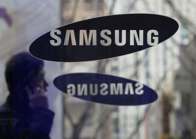 In this Dec. 12, 2013 file photo, a man with a mobile phone walks by the Samsung Electronics logos at its headquarters in Seoul, South Korea. Samsung Electronics said Monday, Nov. 14, 2016, it has agreed to acquire auto-systems maker Harman for $8 billion as the South Korean giant eyes the growing market for connected cars.