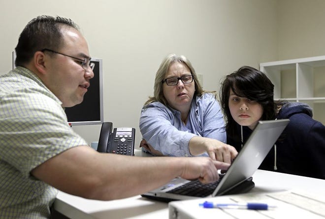 In this Feb. 12, 2015, file photo, enrollment counselor Vue Yang, left, goes over some of the health insurance plans available to Laura San Nicolas, center, accompanied by her daughter, Geena, while enrolling for health insurance at Sacramento Covered in Sacramento, Calif.