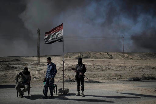 Guards stand at a checkpoint near burning oil fields in Qayara, south of Mosul, Iraq, Tuesday, Nov. 22, 2016. For months, residents of the Iraqi town of Qayara have lived in the darkness from a cloud of toxic fumes released by oil fields lit by retreating Islamic State fighters. (AP Photo/Felipe Dana)
