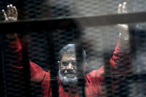 FILE - In this June 21, 2015 file photo, former Egyptian President Mohammed Morsi, wearing a red jumpsuit that designates he has been sentenced to death, raises his hands inside a defendants cage in a makeshift courtroom at the national police academy, in an eastern suburb of Cairo, Egypt. An Egyptian court struck down on Tuesday, Nov. 22, 2016 a life sentence and ordered the retrial of ousted Islamist President Mohammed Morsi on charges of conspiring with foreign militant groups, including the Palestinian Hamas. The decision comes nearly 17 months after the initial sentence against Morsi, who hails from the now-banned Muslim Brotherhood. Along with Morsi's life sentence, those of 16 others, including the group's spiritual leader Mohammed Badei, were thrown out. (AP Photo/Ahmed Omar, File)