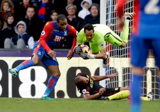 Manchester City's goalkeeper Claudio Bravo, top, lands after colliding with his teammate Vincent Kompany, bottom, as he makes a catch under pressure from Crystal Palace's Jason Puncheon, left, during the English Premier League soccer match between Crystal Palace and Manchester City at Selhurst Park stadium in London, Saturday, Nov. 19, 2016. (AP Photo/Matt Dunham)