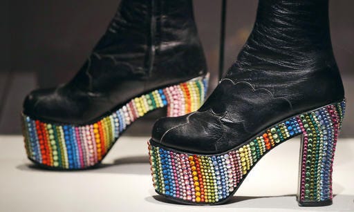 In this Tuesday, Nov. 15, 2016 photo, Elton John's rainbow glass embossed platform boots, designed by Bill Whitten in the 1970's, are displayed at the Peabody Essex Museum in Salem, Mass. From flats to stilettos, what we put on our feet says something about who we are. That’s the premise of new exhibition in Massachusetts. “Shoes: Pleasure and Pain” opens Saturday, Nov. 19, 2016, at the Peabody Essex Museum in Salem. (AP Photo/Charles Krupa)