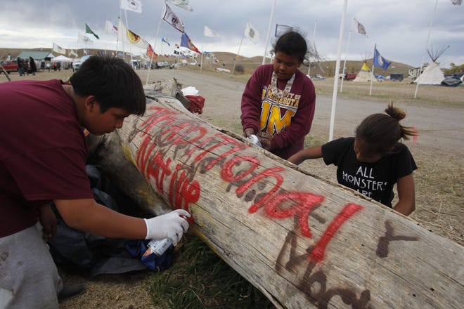 From left to right: Native children Hunter, 12, Rayna, 10, and Frankie, 11, use spray paint to decorate a log with anti-pipeline related messages and designs at the Sacred Stone Camp in Fort Yates, North Dakota.