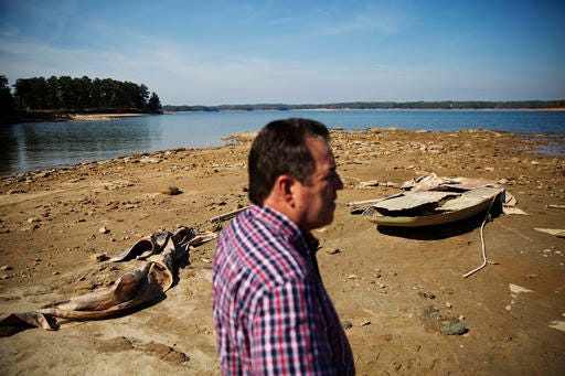 FILE- In this Wednesday, Oct. 26, 2016, file photo, a sunken boat is exposed by receding water levels on Lake Lanier as U.S. Army Corps of Engineers Natural Resources Manager Nick Baggett looks on in Flowery Branch, Ga. Though water shortages have yet to drastically change most people’s lifestyles, southerners are beginning to realize that they’ll need to save their drinking supplies with no end in sight to an eight-month drought. Already, watering lawns and washing cars is restricted in some parts of the South, and more severe water limits loom if long-range forecasts of below-normal rain hold true through the rest of 2016. (AP Photo/David Goldman, File)