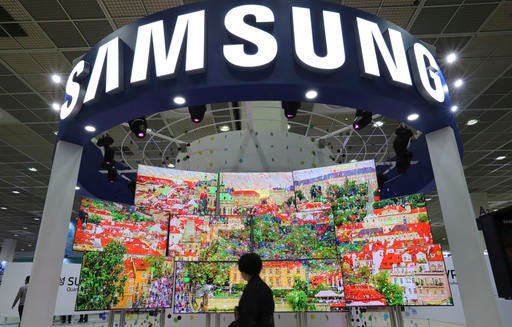 FILE - In this Oct. 26, 2016 file photo, a visitor walks by Samsung Electronics TV screens at Korea Electronics Show or KES in Seoul, South Korea. Samsung Electronics said Tuesday, Nov. 29 it will increase shareholder returns and review its corporate structure as investors step up pressure to reform the South Korean tech giant's governance structure following the Galaxy Note 7 fiasco. (AP Photo/Lee Jin-man, File)
