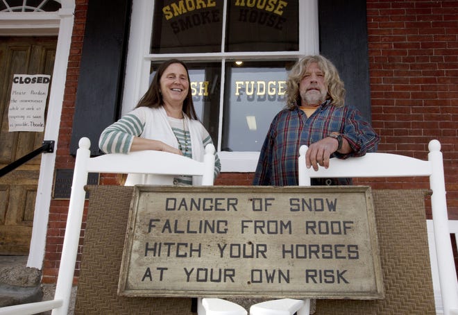 In this photo taken Monday, Nov. 21, Becky and Scott Mitchell pose on the front porch with an old sign they found after purchasing the general store in Bath. In January, its longtime owners closed the store, citing financial difficulties. Becky and Scott Mitchell bought it at auction in July. They hope to reopen soon. In 1985, the store was named to the National Register of Historic Places. (AP Photo/Jim Cole)