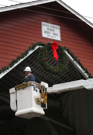 Lane Electric lineman Linc Linebaugh helps Westfir volunteers put up Christmas decorations on the Office Covered Bridge in Westfir in preparation a lighting festival to be held Saturday night. (Chris Pietsch/The Register-Guard)