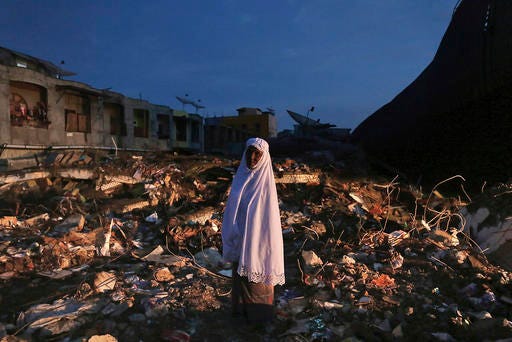 A woman stands on the ruin of a market after Wednesday's earthquake in Meureudu, Aceh province, Indonesia, early Thursday, Dec. 8, 2016. Thousands of people in the Indonesian province of Aceh took refuge for the night in mosques and temporary shelters after a strong earthquake Wednesday killed a large number of people and destroyed dozens of buildings. (AP Photo/Heri Juanda)