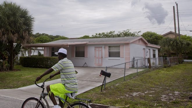 A man rides a bicycle past a house in Riviera Beach. Palm Beach Post File Photo